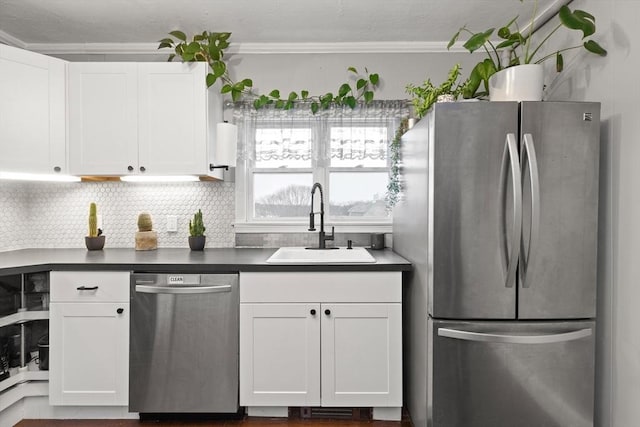 kitchen featuring a sink, appliances with stainless steel finishes, white cabinetry, dark countertops, and backsplash