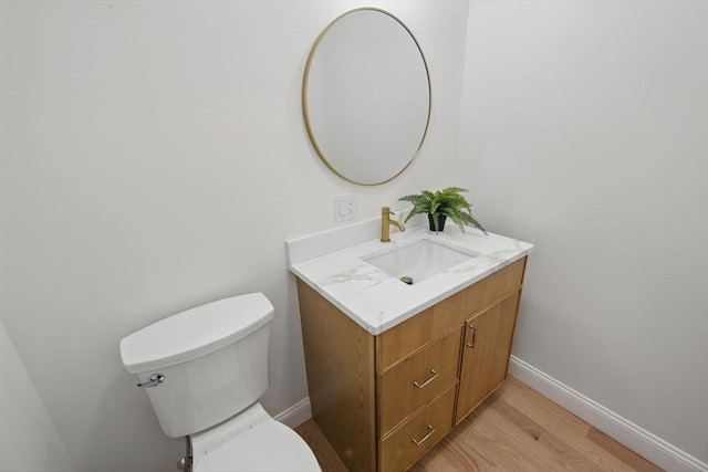 bathroom featuring baseboards, toilet, wood finished floors, and vanity