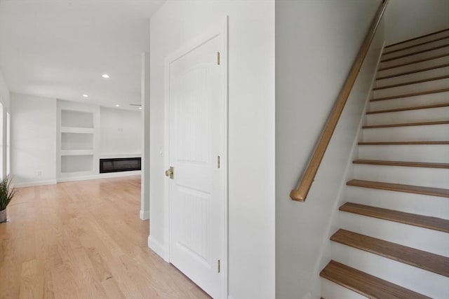 stairs with a glass covered fireplace, built in features, wood finished floors, and baseboards