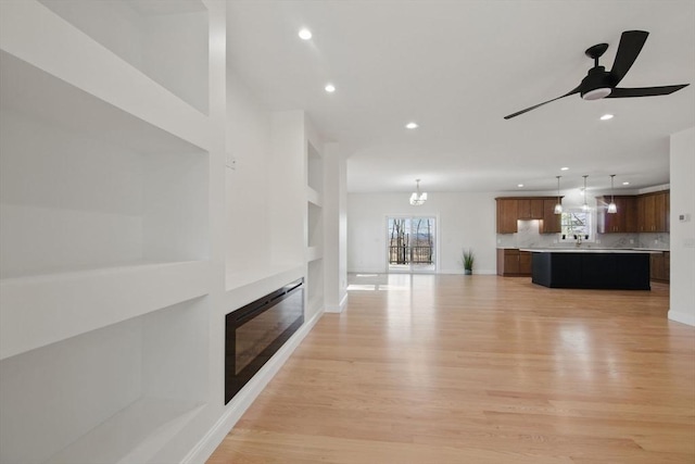 unfurnished living room with light wood finished floors, a glass covered fireplace, recessed lighting, and a ceiling fan