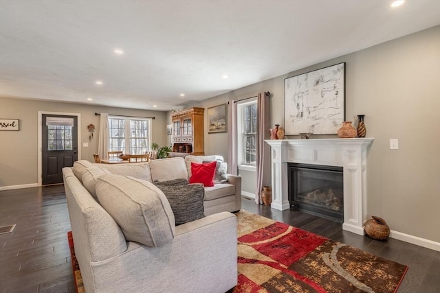 living room featuring a glass covered fireplace, baseboards, dark wood-style floors, and recessed lighting