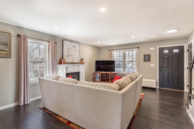 living area featuring a glass covered fireplace, plenty of natural light, dark wood-type flooring, and baseboards