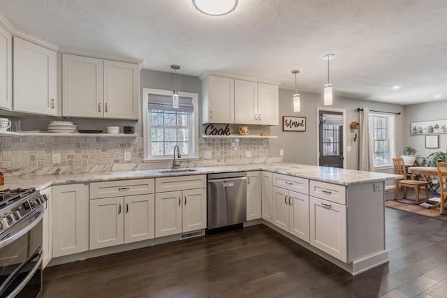 kitchen with dark wood finished floors, appliances with stainless steel finishes, a peninsula, white cabinets, and a sink