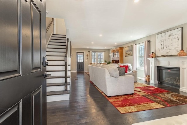 living room featuring stairs, a glass covered fireplace, plenty of natural light, and dark wood-style flooring