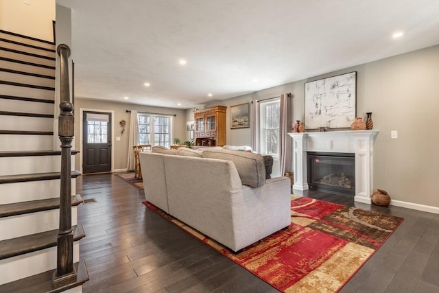 living room with a glass covered fireplace, dark wood finished floors, recessed lighting, stairway, and baseboards