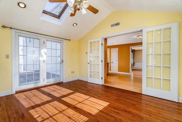 spare room featuring ceiling fan, french doors, baseboard heating, lofted ceiling with skylight, and hardwood / wood-style flooring