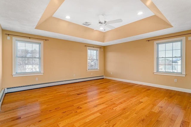 spare room with ceiling fan, a baseboard heating unit, light hardwood / wood-style floors, and a tray ceiling