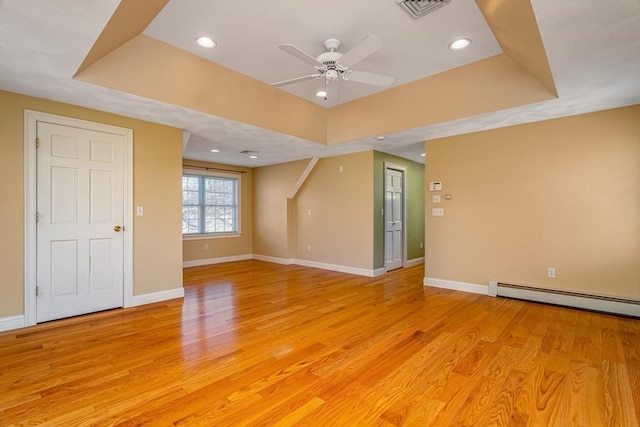 interior space with ceiling fan, light hardwood / wood-style floors, a tray ceiling, and a baseboard radiator