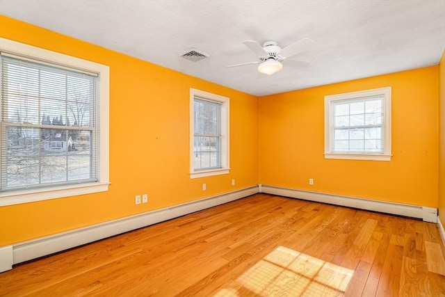 empty room with light wood-type flooring, a baseboard radiator, and plenty of natural light