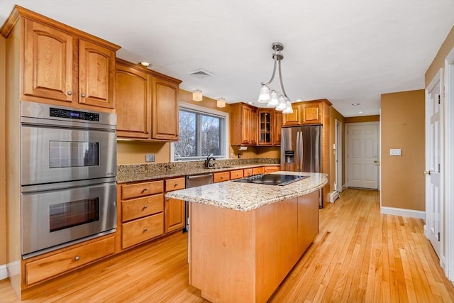 kitchen with light stone counters, stainless steel appliances, sink, a kitchen island, and hanging light fixtures