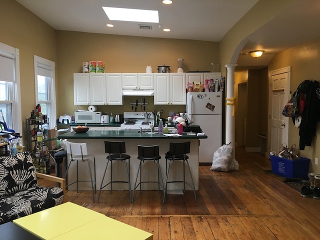 kitchen featuring white appliances, decorative columns, dark wood-type flooring, a breakfast bar, and white cabinets