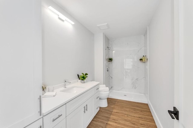 bathroom featuring hardwood / wood-style floors, vanity, a tile shower, and toilet