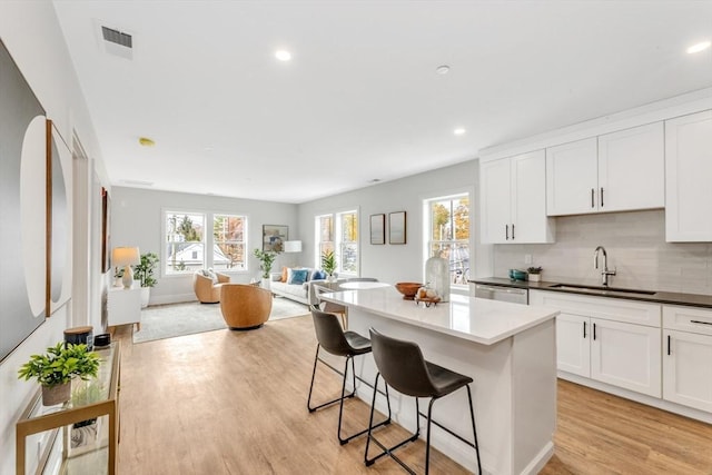 kitchen featuring decorative backsplash, a kitchen breakfast bar, sink, light hardwood / wood-style flooring, and white cabinetry