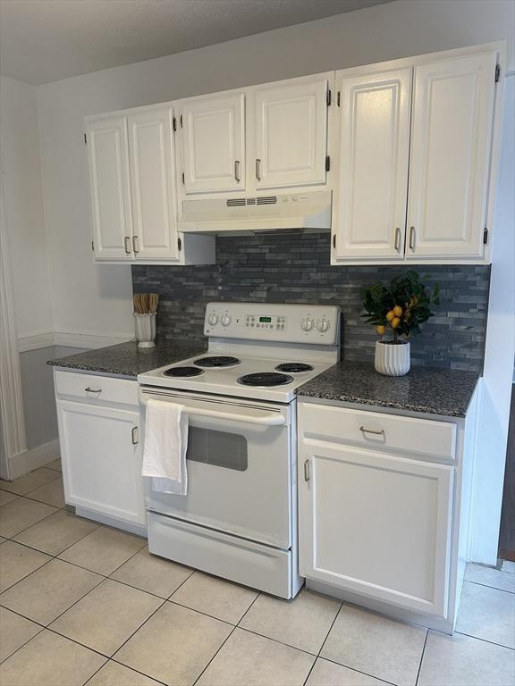 kitchen featuring under cabinet range hood, light tile patterned floors, white range with electric stovetop, and white cabinets