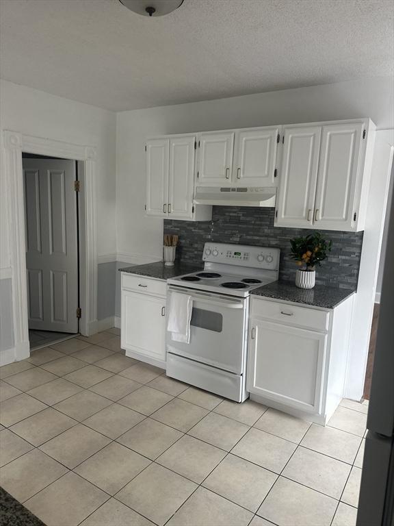 kitchen with tasteful backsplash, electric range, light tile patterned flooring, white cabinetry, and under cabinet range hood