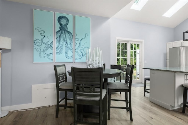 dining room featuring vaulted ceiling with skylight and light hardwood / wood-style floors