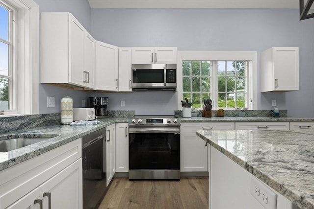 kitchen featuring white cabinets, light hardwood / wood-style floors, light stone countertops, and stainless steel appliances