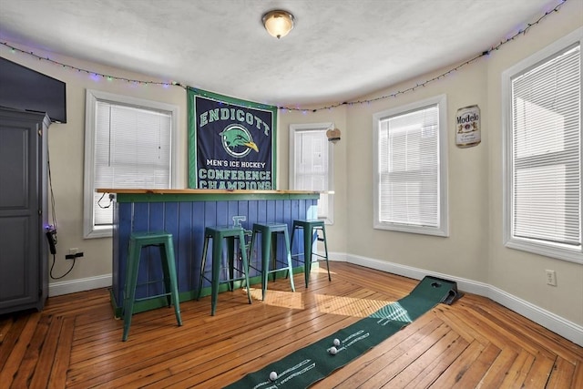 bar with a bar, wood-type flooring, and baseboards