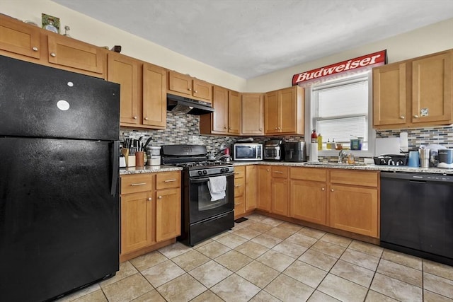 kitchen with tasteful backsplash, a sink, light stone countertops, under cabinet range hood, and black appliances