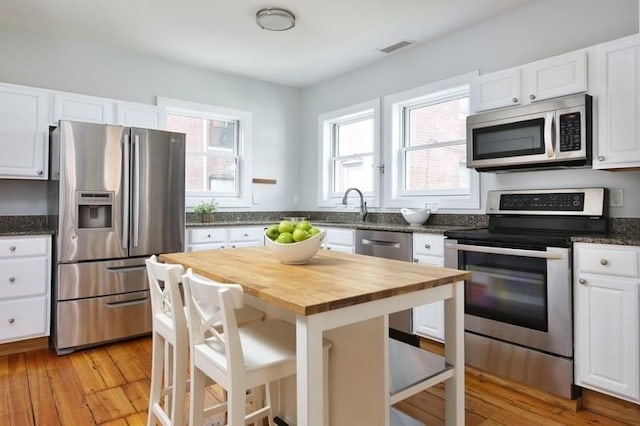 4 Perry St Unit 2, Brookline, MA 02445 - kitchen featuring appliances with stainless steel finishes, wood counters, white cabinetry, a breakfast bar, and light wood finished floors