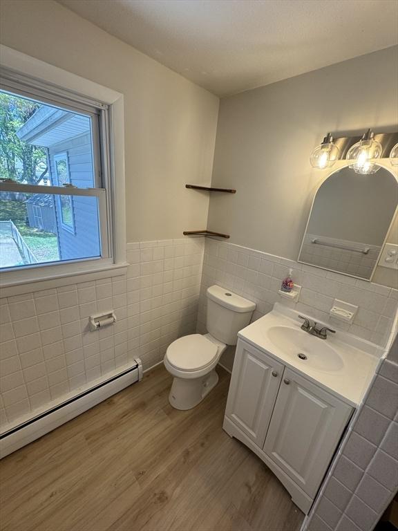 bathroom with a baseboard radiator, tile walls, toilet, and wood finished floors