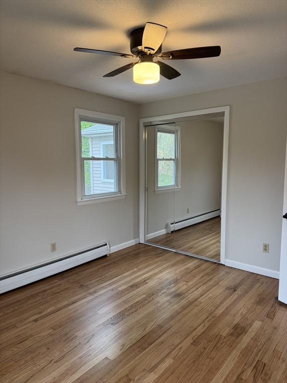 spare room featuring a healthy amount of sunlight, baseboard heating, and wood finished floors