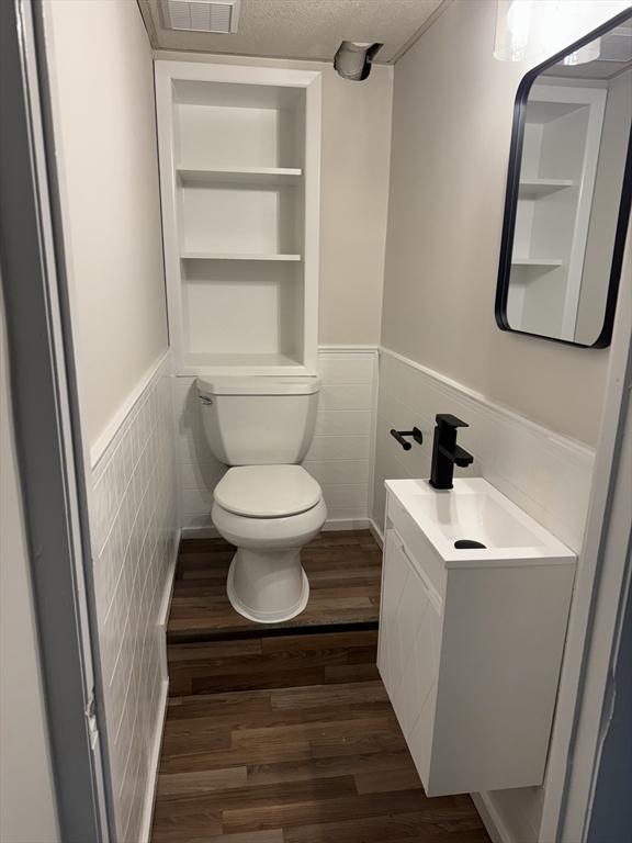 half bathroom featuring toilet, wood finished floors, vanity, built in features, and wainscoting