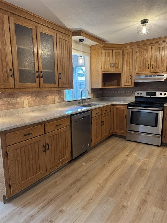 kitchen featuring a sink, brown cabinets, light wood-type flooring, under cabinet range hood, and appliances with stainless steel finishes