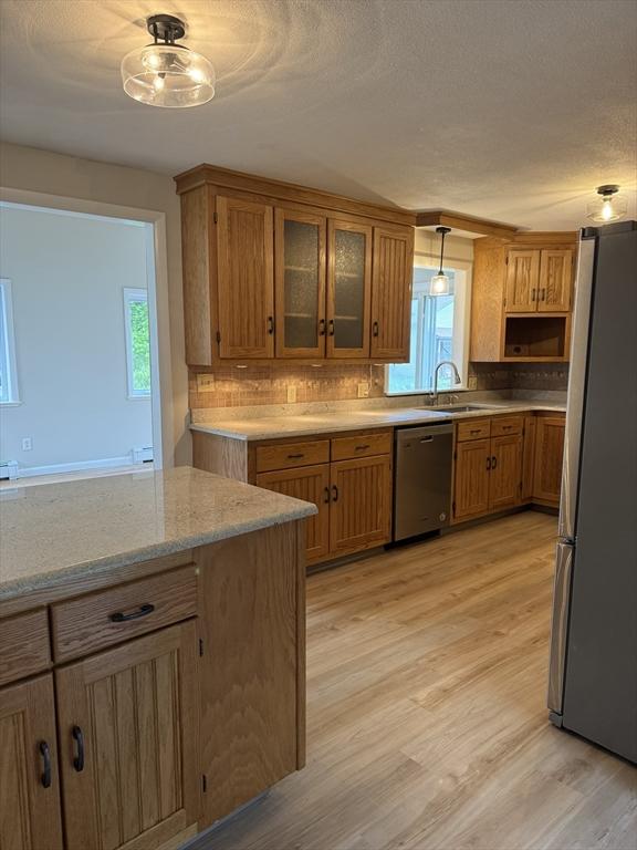 kitchen with plenty of natural light, brown cabinetry, backsplash, stainless steel appliances, and light wood-type flooring