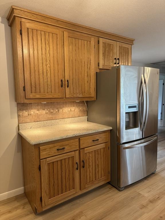 kitchen featuring light wood finished floors, brown cabinetry, and stainless steel fridge with ice dispenser
