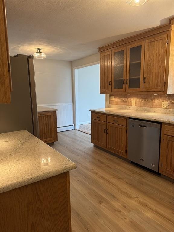 kitchen featuring glass insert cabinets, stainless steel appliances, brown cabinetry, light wood-type flooring, and wainscoting