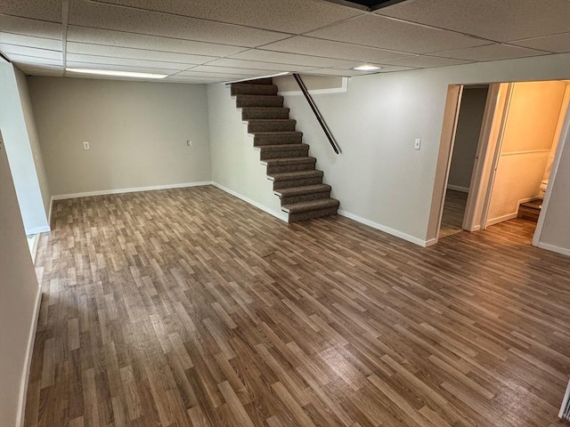 finished below grade area with a drop ceiling, stairway, and wood finished floors