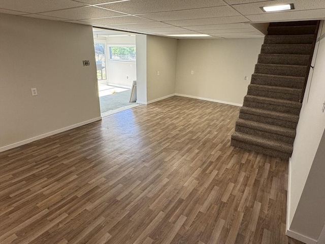 basement featuring dark wood finished floors, stairs, baseboards, and a paneled ceiling
