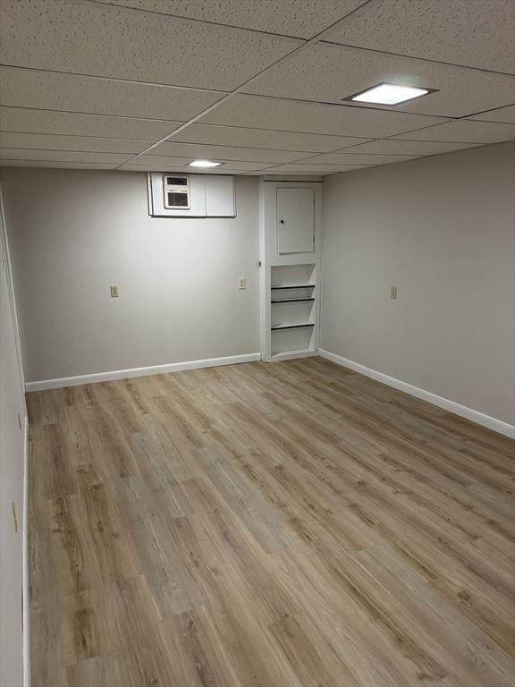 finished below grade area featuring light wood-style floors, a drop ceiling, and baseboards