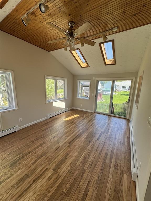 spare room featuring vaulted ceiling with skylight, wood finished floors, track lighting, and a baseboard heating unit