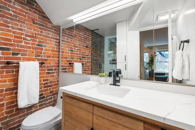 bathroom featuring toilet, vaulted ceiling, vanity, and brick wall