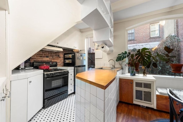 kitchen featuring decorative backsplash, freestanding refrigerator, white cabinetry, a sink, and gas stove