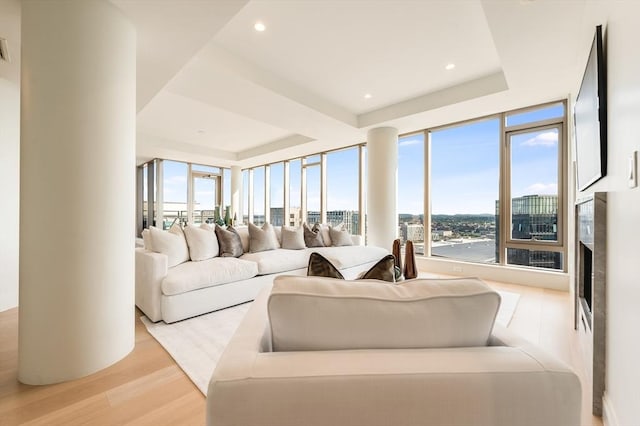 living room with a wall of windows, recessed lighting, a raised ceiling, light wood-style flooring, and a premium fireplace