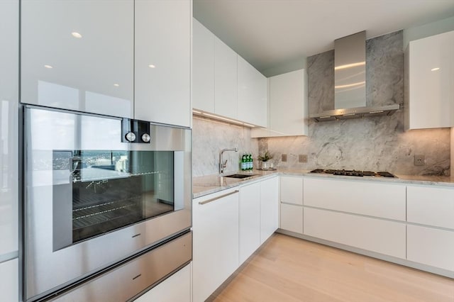 kitchen featuring gas cooktop, a sink, wall chimney exhaust hood, and white cabinets