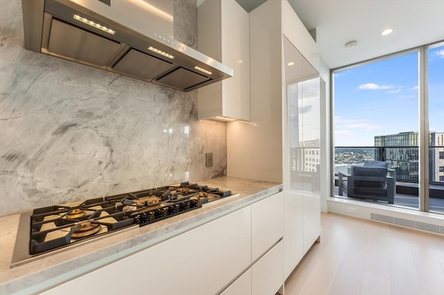 kitchen featuring white cabinets, modern cabinets, a healthy amount of sunlight, and wall chimney range hood