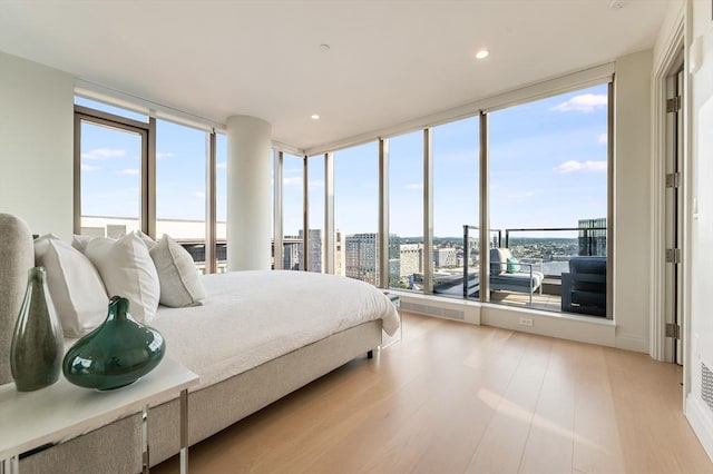 bedroom with light wood-type flooring, a city view, recessed lighting, and a wall of windows