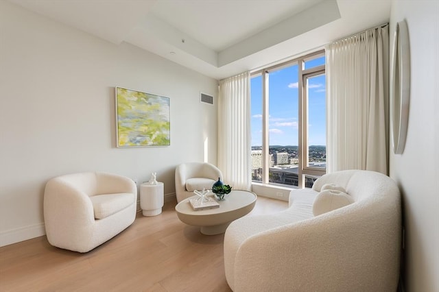 sitting room with baseboards, visible vents, wood finished floors, and a raised ceiling