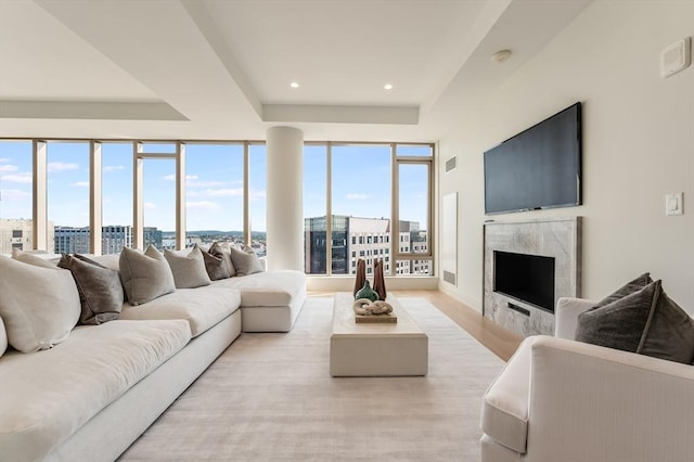 living area featuring visible vents, a fireplace, a raised ceiling, light wood-style floors, and recessed lighting