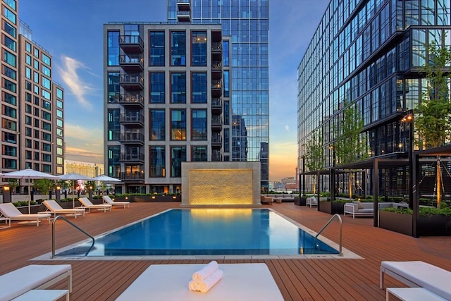 pool at dusk featuring a community pool, a wooden deck, and a city view