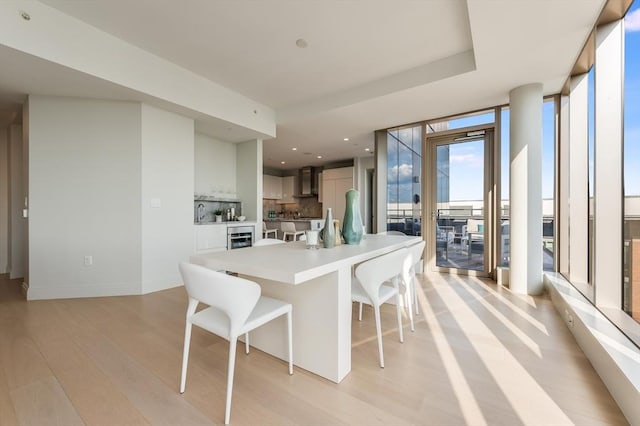 kitchen with light countertops, light wood-style flooring, wall chimney exhaust hood, decorative backsplash, and a kitchen bar
