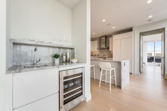 bar featuring decorative backsplash, beverage cooler, indoor wet bar, wall chimney range hood, and a sink