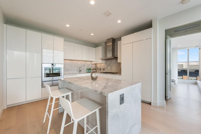 kitchen with appliances with stainless steel finishes, tasteful backsplash, a warming drawer, a breakfast bar, and wall chimney exhaust hood
