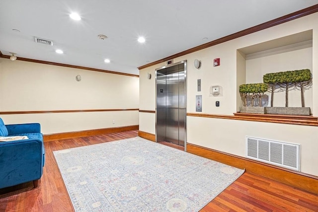 sitting room featuring elevator, ornamental molding, and hardwood / wood-style floors