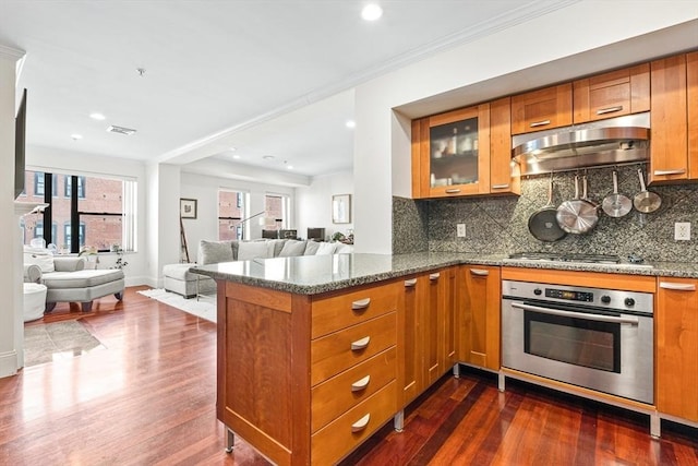 kitchen featuring dark wood-type flooring, stainless steel appliances, kitchen peninsula, and tasteful backsplash