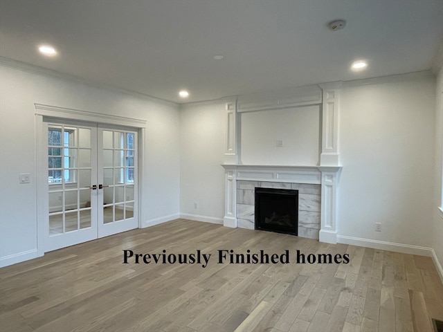 unfurnished living room featuring french doors, light wood-type flooring, a tiled fireplace, and crown molding